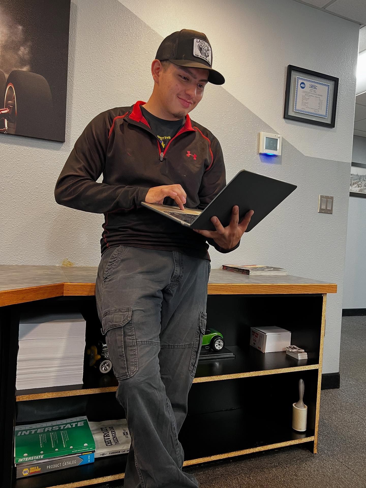 A technician running a digital inspection on a laptop beside the shop's ASE certification