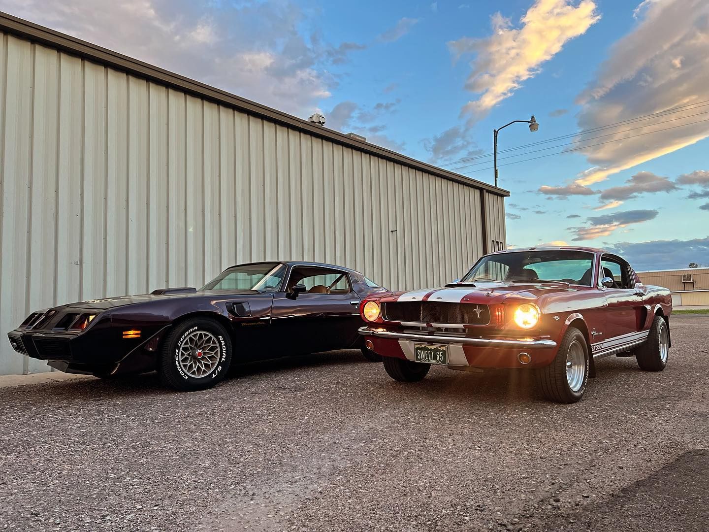 A restored Trans Am and a 1965 Mustang fastback parked outside Gearheadz Garage at sunset